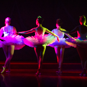 Group of ballerinas on pointe, white costumed bathed in multicoloured stage lights