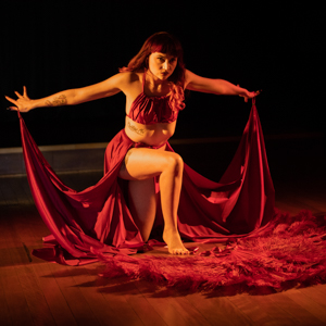 Dancer Rosetta Stirling in dramatic pose on one knee in a red costume with feather fans