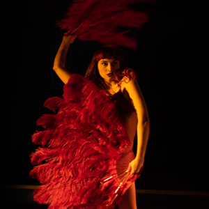 Dancer Rosetta Stirling standing in a dramatic pose hiding her body with red feather fans