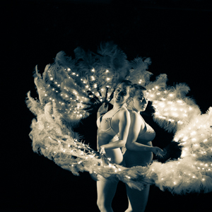 Two dancers standing back to back framing themselves with feather fans. 