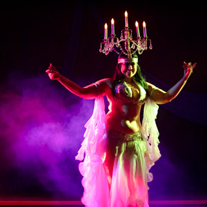 Bellydancer with shammadam candelebra on her head, pink lights through smoke onstage.
